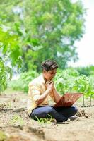 Indian boy studying in farm, holding laptop in hand , poor indian kids photo
