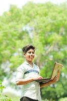 Indian boy studying in farm, holding laptop in hand , poor indian kids photo