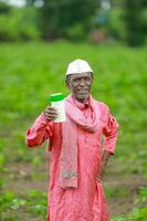 Indian happy farmer holding empty Bottle in hands, happy farmer showing white Bottle photo