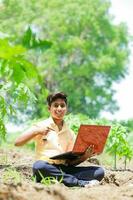 Indian boy studying in farm, holding laptop in hand , poor indian kids photo