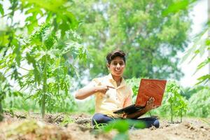 Indian boy studying in farm, holding laptop in hand , poor indian kids photo