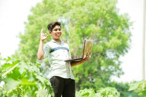 Indian boy studying in farm, holding laptop in hand , poor indian kids photo