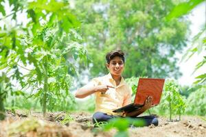 Indian boy studying in farm, holding laptop in hand , poor indian kids photo