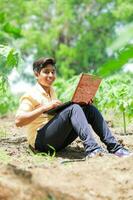 Indian boy studying in farm, holding laptop in hand , poor indian kids photo