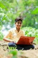 indio chico estudiando en granja, participación ordenador portátil en mano , pobre indio niños foto