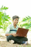 indio chico estudiando en granja, participación ordenador portátil en mano , pobre indio niños foto