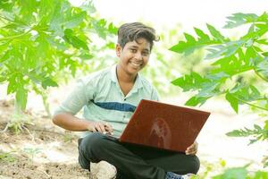 Indian boy studying in farm, holding laptop in hand , poor indian kids photo