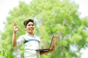 Indian boy studying in farm, holding laptop in hand , poor indian kids photo