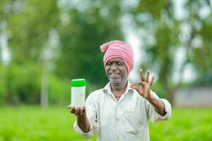 Indian happy farmer holding empty Bottle in hands, happy farmer showing white Bottle photo