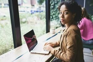 Young african woman doing school assignment on her laptop in cafeteria photo