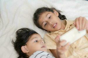 Little boy and his older sister are play smart phone on a bed at home. photo