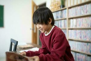 Cute little boy reading book School child pupil reading book at school. Kid doing homework, sitting at table by books, ienjoying interesting stories, reading fascinating adventurous novels, copy space photo