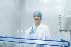 Portrait thumbs up of smiling Caucasian technologist expert standing by an automated machine for PET water production in a bottling factory. photo