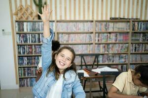 retrato de linda rubia niña levantamiento mano para responder mientras sentado a escritorio en colegio aula, Copiar espacio foto