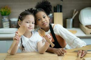 Two little girls in the kitchen prepare food, a dessert for the family. As they learn to cook they start playing with flour and smiling each other. Concept of cooking classes, family, education. photo