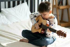 gracioso chico niño jugando guitarra a hogar foto