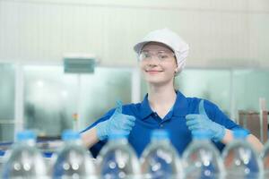 Portrait thumbs up of smiling Caucasian technologist expert standing by an automated machine for PET water production in a bottling factory. photo