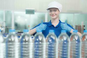 Portrait thumbs up of smiling Caucasian technologist expert standing by an automated machine for PET water production in a bottling factory. photo