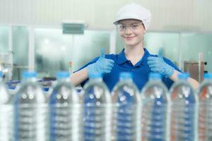 Portrait thumbs up of smiling Caucasian technologist expert standing by an automated machine for PET water production in a bottling factory. photo