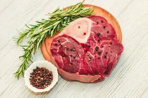 Fresh piece of meat large beef steak on the bone ossobuco with pepper, rosemary on the board photo