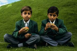 dos joven Niños en colegio uniformes disfrutando un bocadillo en el césped foto