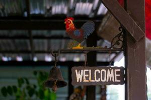 A welcome plaque with hanging bells and a rooster statue above. It's a classic badge. photo