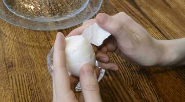 Woman peeling boiled egg on wooden background photo