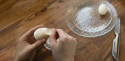 Woman peeling boiled egg on wooden background photo