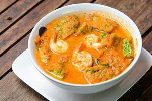 Spicy tamarind soup with veggies and shrimp on the wooden background. photo