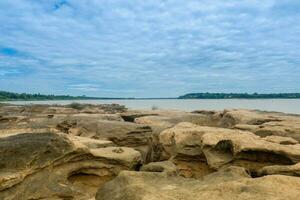 Brown rock rapids beside the big river There are clouds in the sky during the day. photo