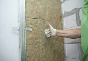 The worker insulates the walls with mineral wool for further cladding with plasterboard. Heat insulation and sound insulation of housing photo