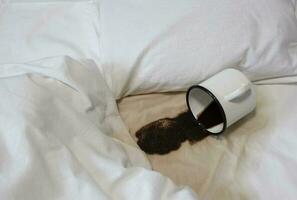 A spilled cup of coffee on the bed. A cup accidentally fell on a white sheet. Bad, bad breakfast. A wet spot. photo