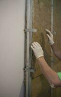 Installing mineral fiber glass wool between beams framing the wall in order to provide thermal and sound insulation. photo