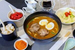 Japanese curry with udon noodle and crispy pork chop croquettes and boiled egg topping on bowl cup style. photo