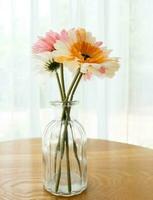 The artificial flower in the clear glass vase on the wooden table. photo