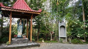 estatua de el Virgen María debajo un pabellón con arboles en el fondo, en el jatiningsih maria cueva, jogjakarta, dónde católicos orar, dar Gracias y enviar peticiones a Dios foto