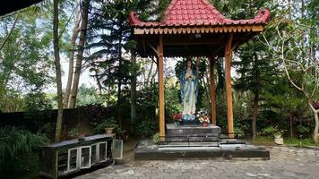 Statue of the Virgin Mary under a canopy with trees in the background, in the Jatiningsih Maria Cave, Jogjakarta, where Catholics pray, give thanks and submit requests to God photo