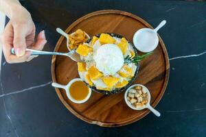 Shaved ice dessert with mango slices. Served with vanilla ice cream and whipped cream. Sweet dessert in Korean style. Local name, Bingsu. photo