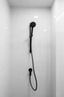 Black shower head on holder against tiled wall on background. Concept of white bathroom in modern Condo photo