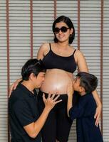 un embarazada madre vestido en negro vistiendo lentes con su marido y hijo. foto