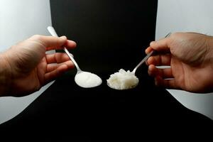 1 spoon of rice and 1 spoon of sugar Same amount of calories each day, two spoons, isolate black background photo