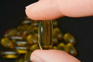 Fish oil in clear yellow capsules. For taking supplements, on male hands, isolate, black background photo