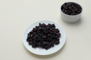 Dried Cranberries On White Plate On Beige Background. Superfood. Selective Focus. Sweet Dehydrated Cranberries. Nutrients And Vitamins. Horizontal Plane. photo