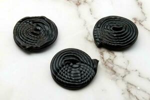 Tasty black licorice candies on white marble background photo