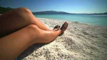 Beine von ein Frau Sonnenbaden im das Sonne auf das Weiß Strand im Meer Urlaub video