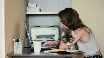 A young Caucasian girl is sitting and stroking a cat at the workplace. Remote work. video