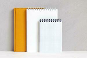 Notebooks are on shelf near gray wall. Empty sheet, mockup, copy space. photo