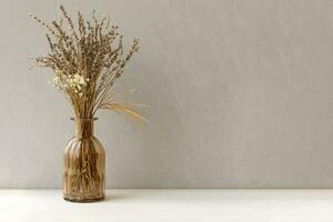 Minimalistic composition of dried flowers in glass brown vase on gray vintage textured wall background and on wooden shelf. Front view, mock up, copy space. photo