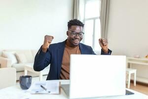 Excited African American man wearing headphones reading good news in email, getting new job, promotion, using laptop, looking at screen and screaming with joy, showing yes gesture, celebrating photo