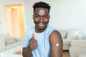 retrato de un hombre sonriente después consiguiendo un vacuna. africano hombre participación abajo su camisa manga y demostración su brazo con vendaje después recepción vacunación. foto